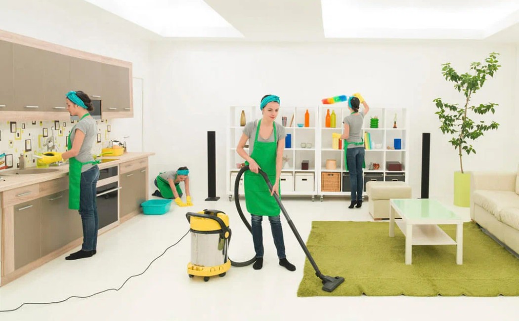 Professional team providing Residential Cleaning Services by vacuuming floors, washing dishes, mopping surfaces, and dusting shelves in a bright, modern home.