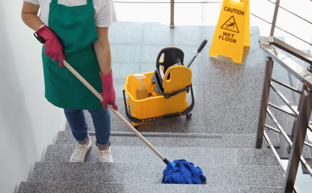 Commercial Cleaning Services worker mopping a staircase with a safety caution sign and cleaning equipment nearby.