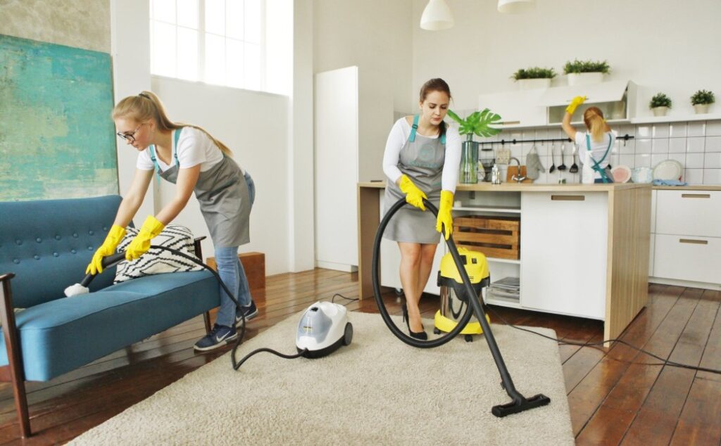 Team of professionals providing Residential Cleaning Services by vacuuming carpets, cleaning furniture, and wiping kitchen surfaces in a modern home interior
