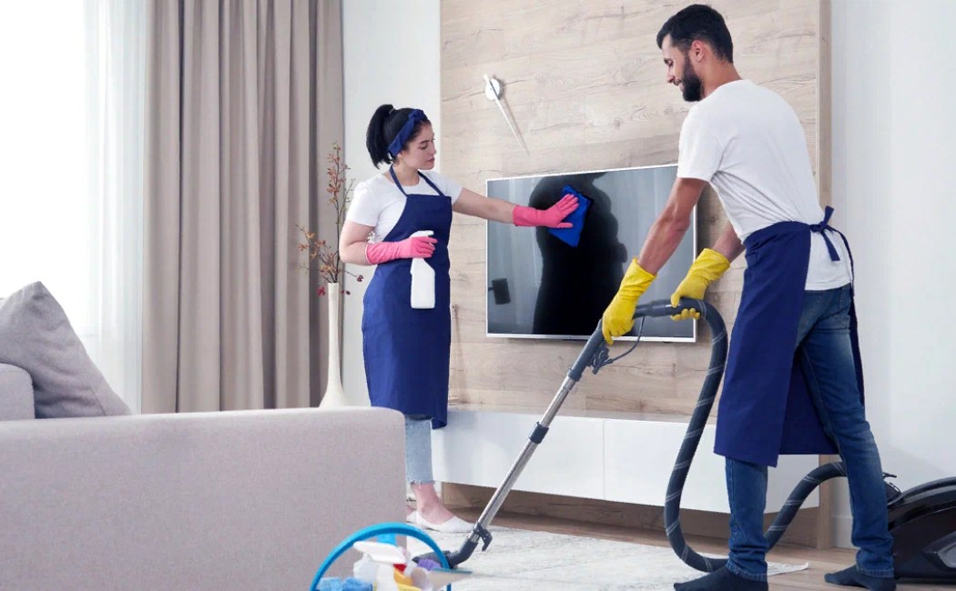 Apartment cleaning Experts vacuuming floors and wiping a TV screen in a modern living room.
