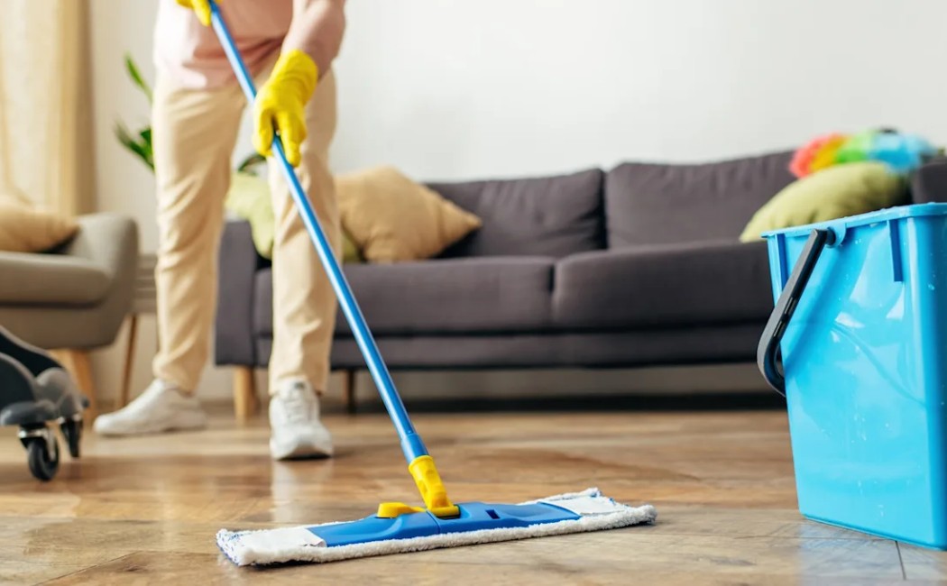 Cleaning professional mopping a hardwood floor in a modern living room with cleaning supplies and equipment nearby.