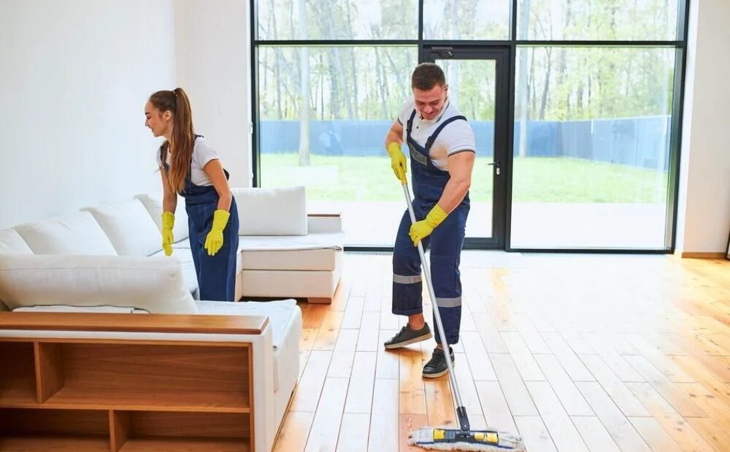Residential Cleaning team mopping hardwood floors and tidying furniture in a bright, modern living room.