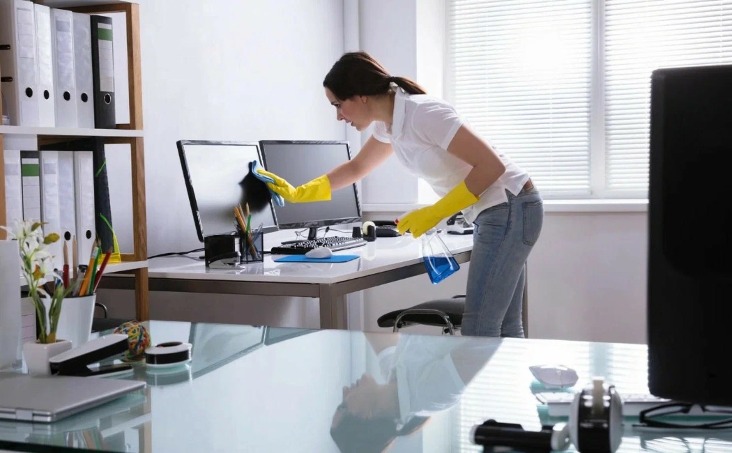Office Cleaning Services specialist disinfecting computer monitors and workstations in a bright, organized office environment.