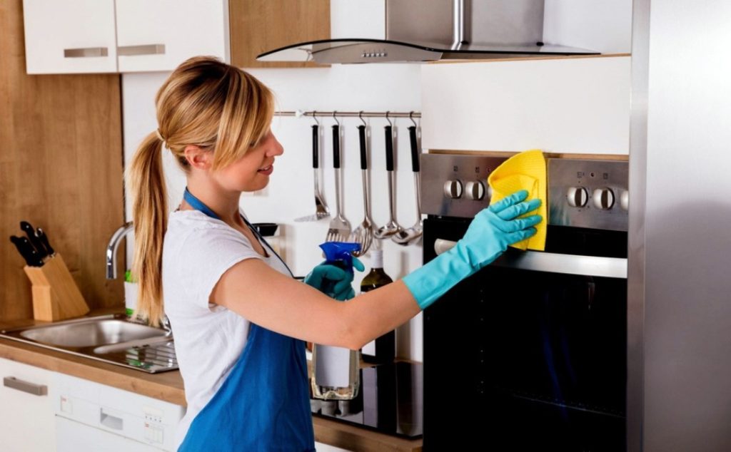 Kitchen Cleaning professional wiping and disinfecting a modern oven in a clean residential kitchen while wearing protective gloves.