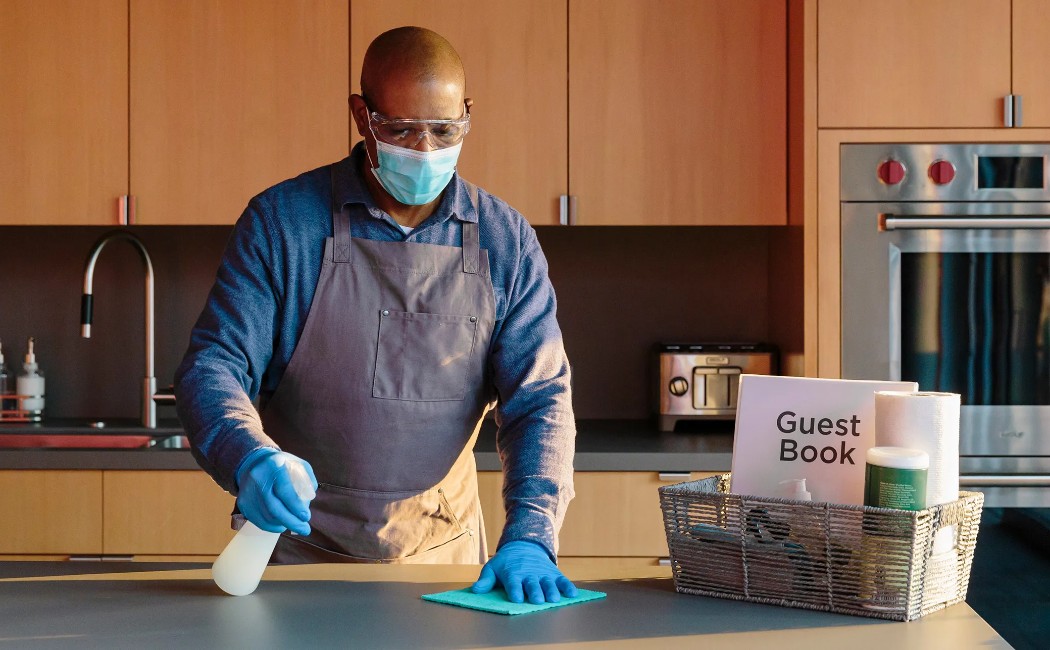 Airbnb cleaning specialist disinfecting a modern kitchen countertop while preparing a vacation rental for incoming guests.