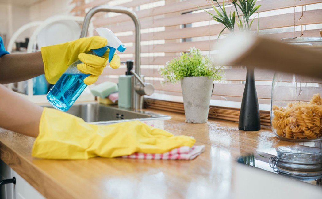 Kitchen cleaning expert using disinfectant spray to clean a modern kitchen worktop and sink area.