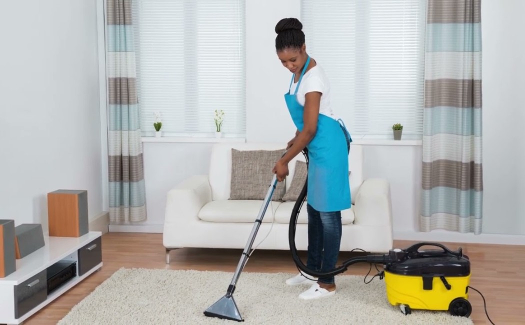 Residential cleaning expert using a vacuum cleaner to deep clean a living room carpet in a bright and well-maintained home.