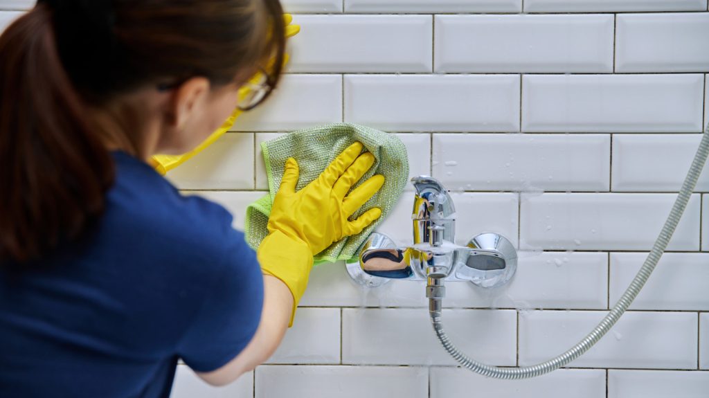 A skilled cleaner wearing yellow gloves uses a cloth to deep clean bathroom tiles and fixtures, removing dirt and grime for a sparkling finish.