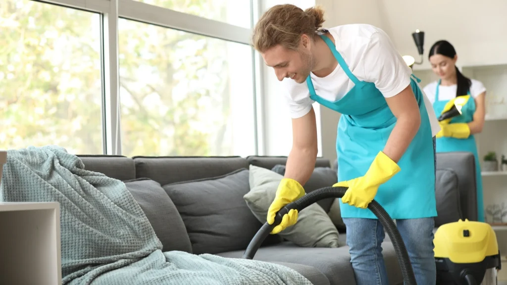 Home Cleaning Service for a Fresh Living Room Sofa Home Cleaning Service professionals are vacuuming a modern living room sofa for a fresh, spotless, and comfortable home.